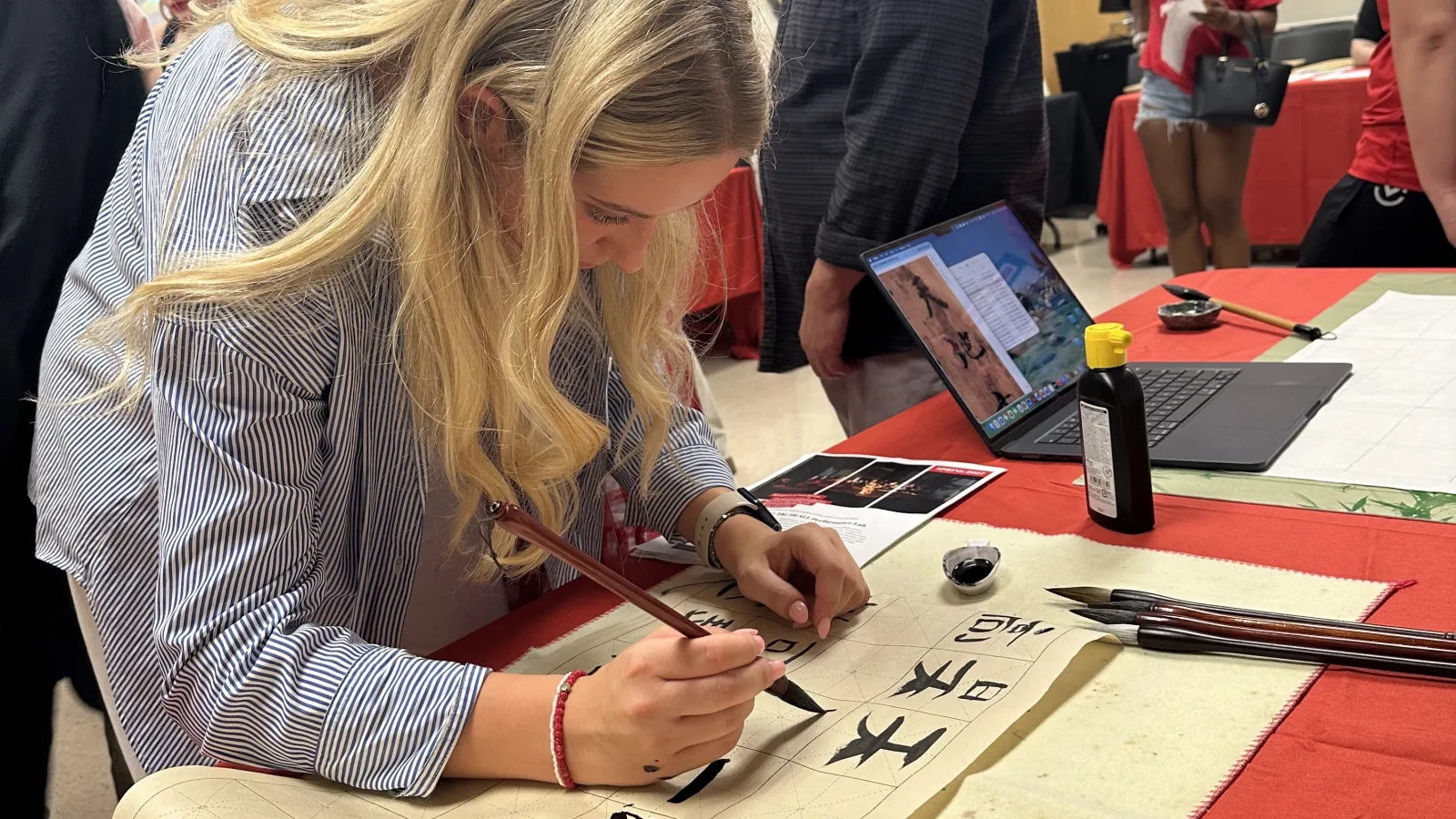 Woman intently doing Chinese caligraphy with a brush and black ink