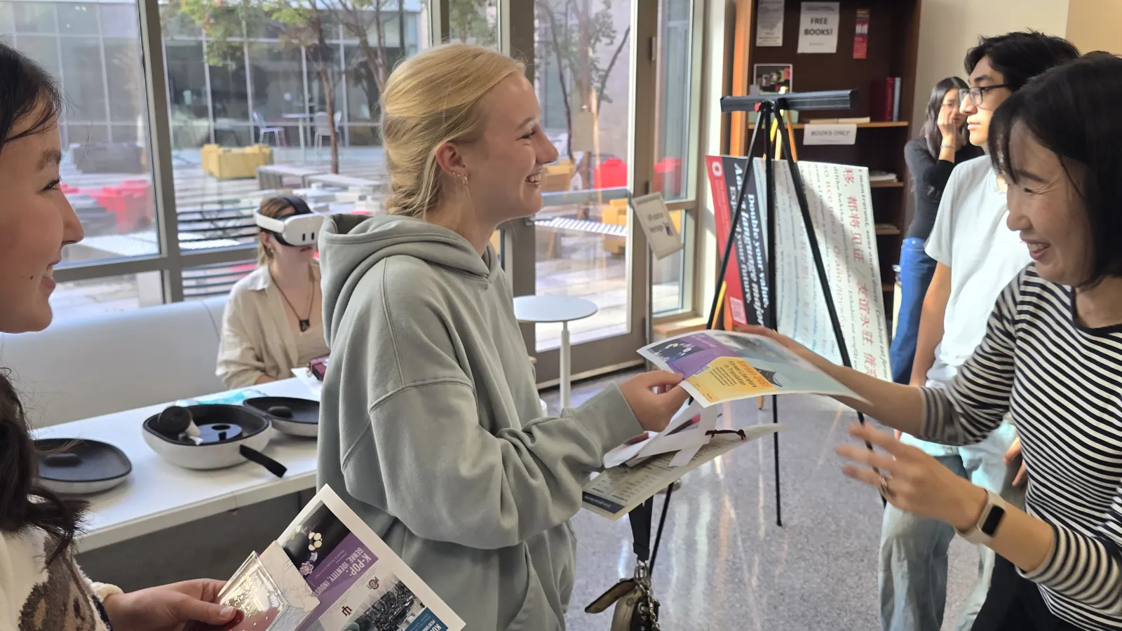 A professor talks to 2 students and hands them course flyers