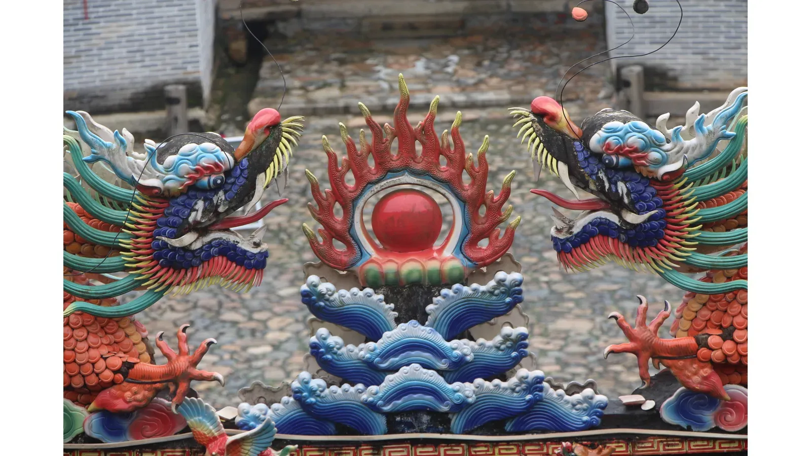 Ornate symmetrical Asian-style architectural decoration with two colorful dragon-like creatures flanking a central red flaming orb above blue waves.