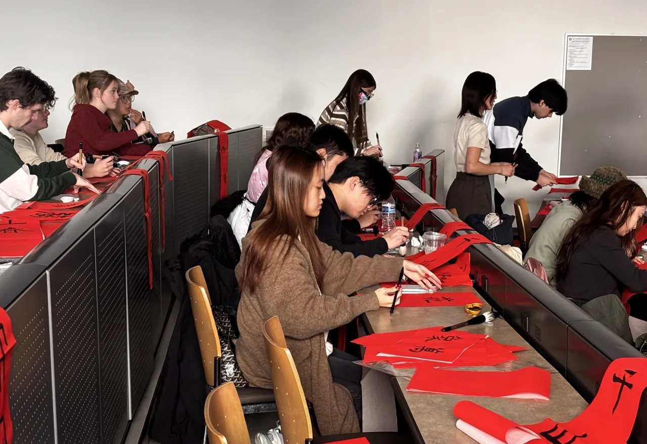 1. A group of people seated at desks, each working with sheets of red paper in a collaborative environment.  