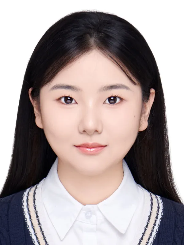 A young woman wearing a white collared shirt and a blue sweater vest standing confidently with a smile.