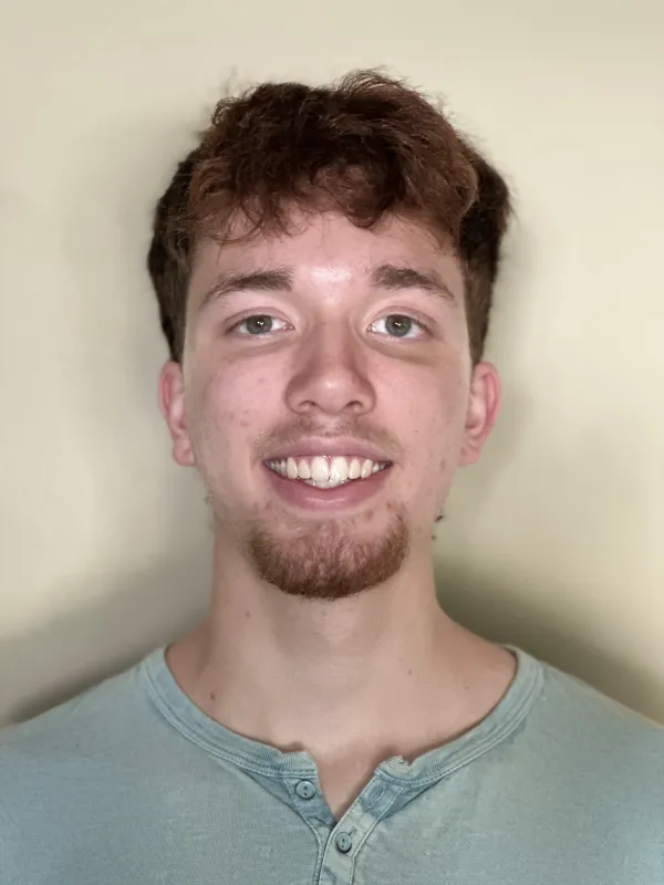 Portrait of a young man with short, curly brown hair and a light green Henley shirt