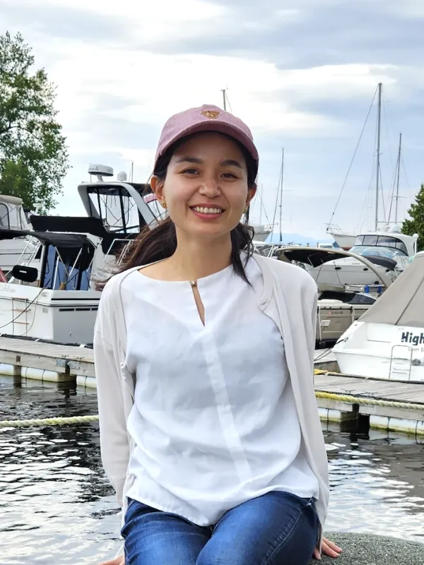 A woman sits on a rock by a marina, surrounded by boats and water, enjoying the serene view