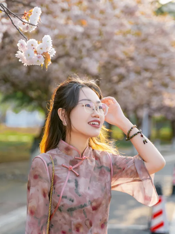 A woman wearing glasses and a floral dress stands in front of a tree, smiling and enjoying the outdoors.  
