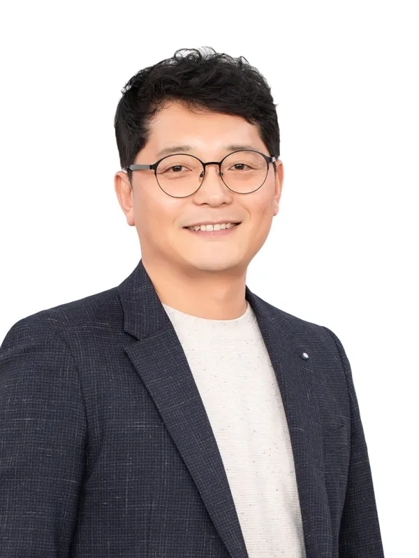 A man wearing glasses and a suit smiles warmly at the camera.  