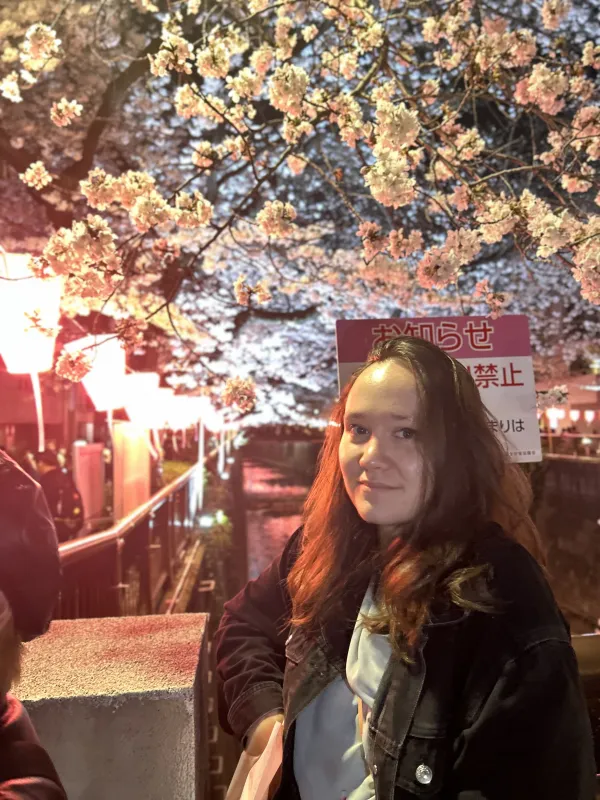A woman relaxes in front of a cherry blossom tree, with its lush pink blossoms framing her peaceful moment.